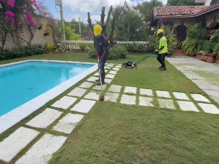 Deux employés TropiClean entretenant la pelouse et les abords d'une piscine
